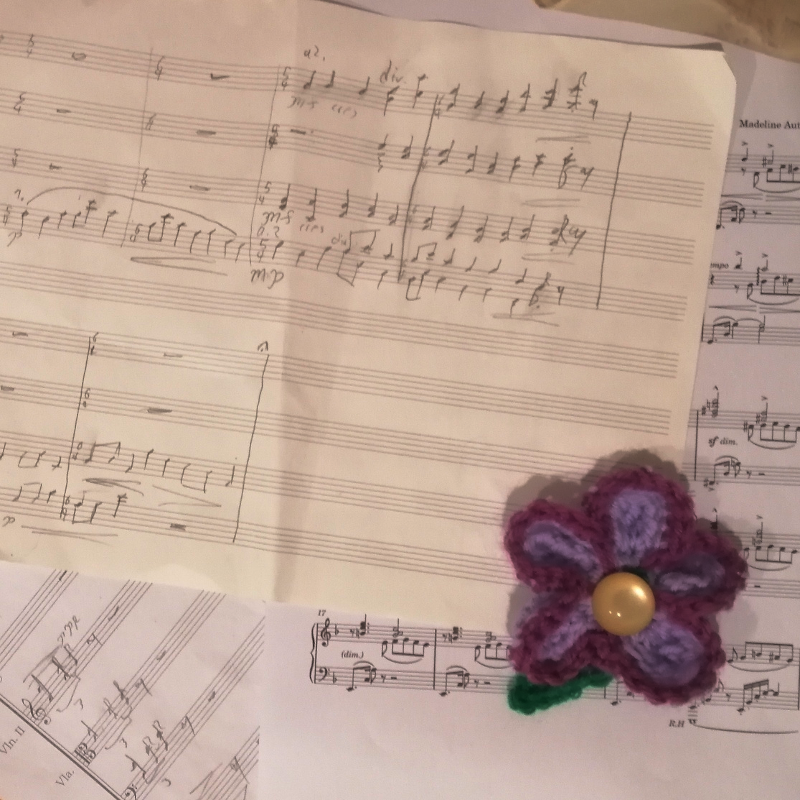 A series of handwritten and engraved scores, with a five-petal crochet flower in purple